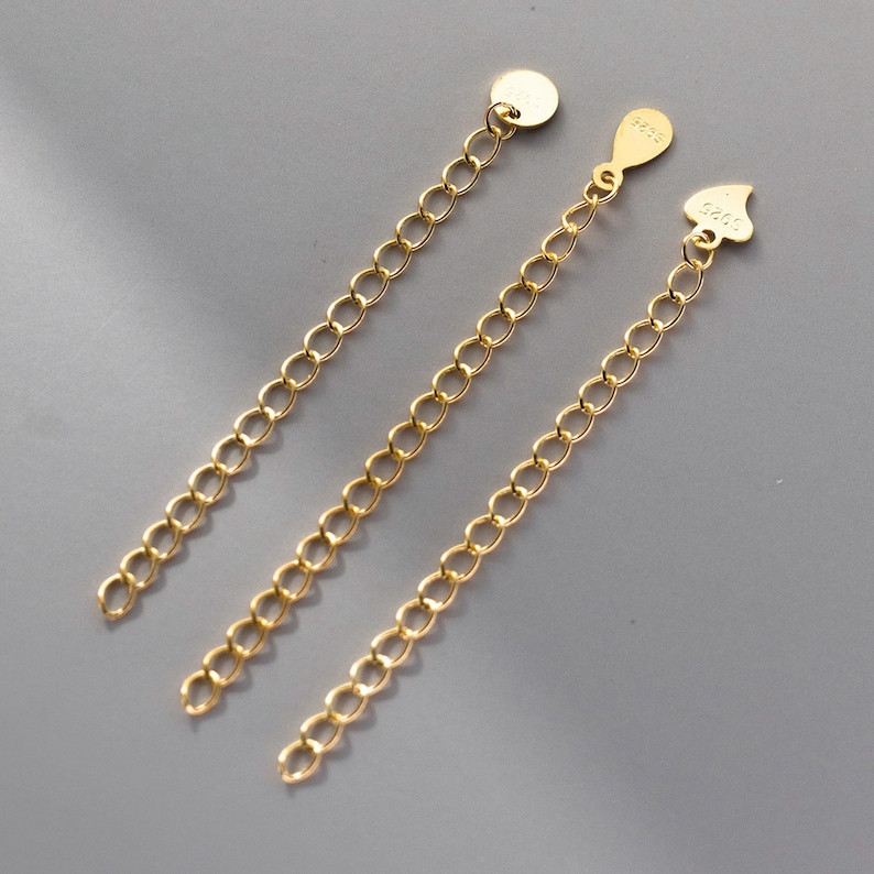 May include: Three gold chain extenders with different end pieces. One has a round end, one has a heart-shaped end, and one has a teardrop-shaped end.