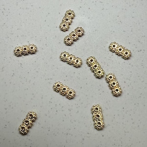 May include: A group of ten gold-colored metal bead spacers. Each spacer is made of four connected circles with a textured surface.