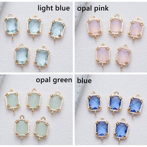 May include: Six gold-toned metal charms with a loop at the top and a square-shaped glass stone in the centre. The stones are in four colours: light blue, opal pink, opal green, and blue.