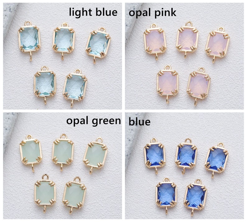 May include: Six gold-toned metal charms with a loop at the top and a square-shaped glass stone in the centre. The stones are in four colours: light blue, opal pink, opal green, and blue.