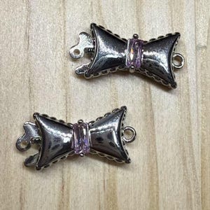 May include: Two silver-toned bow-shaped clasps with a pink rhinestone in the center of each bow.