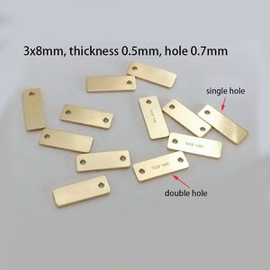 Könnte beinhalten: Eine Gruppe von 10 rechteckigen Metall-Etiketten in Goldfarbe mit zwei verschiedenen Locharten. Einige Etiketten haben ein einzelnes Loch, während andere zwei Löcher haben. Die Etiketten sind 3 mm x 8 mm groß, 0,5 mm dick und haben ein 0,7 mm Loch.