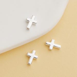 Könnte beinhalten: Drei silberne Kreuz-Anhänger, jeder mit einem einfachen, flachen Design. Die Anhänger sind klein und zart, perfekt, um Schmuck mit einem Hauch von Glauben zu versehen.