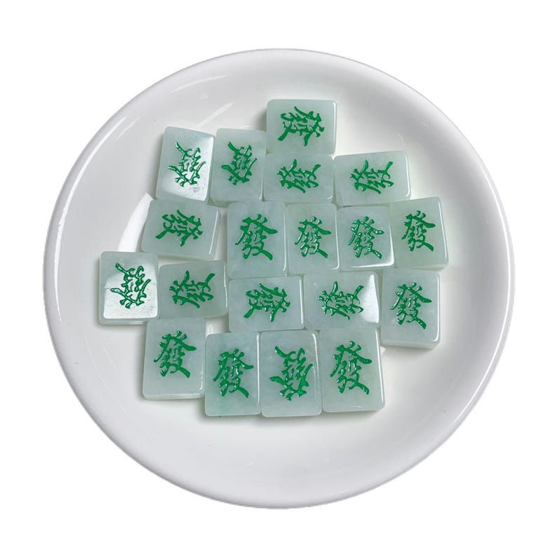 May include: A white ceramic dish with a pile of green and white jade mahjong tiles. The tiles have Chinese characters on them.