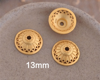 May include: Three gold-toned metal bead caps with intricate designs. Each cap has a small hole in the center and measures 13mm in diameter. The caps are on a light brown surface.