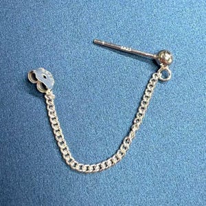 May include: Silver chain earring with a small ball at the end and a heart-shaped charm. The chain is attached to a post that goes through the ear.