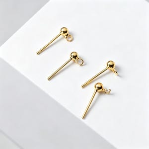 Puede incluir: Cuatro postes para pendientes en tono dorado, cada uno con una pequeña esfera en la parte superior y una diminuta anilla abierta en el lateral para la creación de joyas. Estos fornituras metálicas tienen un acabado liso y pulido.