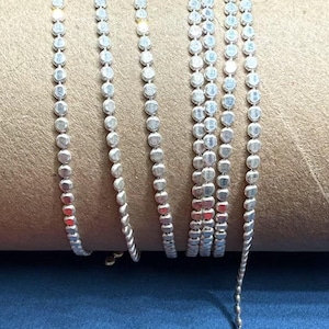 May include: Silver chain with small, round links. The chain is coiled on a brown surface.