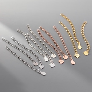 May include: A set of eight silver, gold, and rose gold chain extenders with different charms. The charms include a teardrop and a heart shape. Each charm has the number "925" engraved on it.