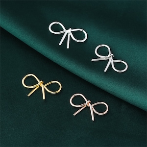 May include: Four bow-shaped earrings in silver, gold, and rose gold. The earrings are simple and elegant, and would make a great gift.