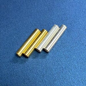 May include: Four metal tubes, two gold and two silver, arranged in a staggered pattern on a blue surface.