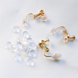 Peut inclure: Ensemble de composants de boucles d'oreilles à clipser dorés et de coussinets d'oreille en silicone transparent. Les boucles d'oreilles ont un design à levier avec un petit coussinet rond pour le confort. Les coussinets sont éparpillés.