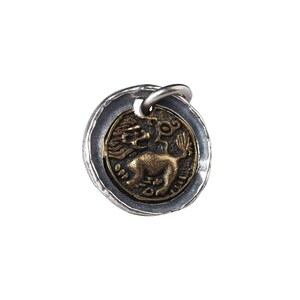 May include: A silver and gold pendant featuring a stylised lion with wings and a tail ending in a flower. The pendant is round and has a textured silver border.