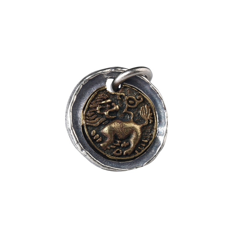 May include: A silver and gold pendant featuring a stylised lion with wings and a tail ending in a flower. The pendant is round and has a textured silver border.