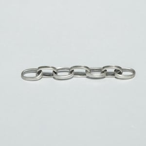 May include: A section of a silver-colored chain with oval links. The chain is laid out horizontally against a white background. The links are uniform in size and shape, with a slightly rounded profile.