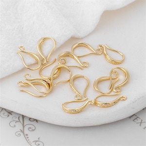 May include: A collection of gold-colored jewelry clasps, hooks, and findings. The clasps have a curved design with a decorative pattern on the hook end. They are arranged on a white surface, suggesting a craft or jewelry-making theme.