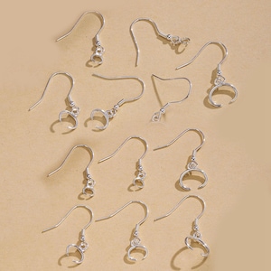 May include: A collection of silver-colored earring hooks in various styles. Some hooks have a simple curved design, while others feature decorative elements like small beads or a circular loop for attaching charms. The hooks are arranged on a neutral background.