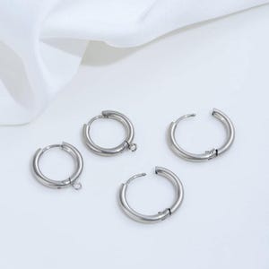 May include: Four silver-toned metal hoop earrings arranged in a cluster. Each hoop features a hinged closure mechanism and a small circular loop attached to the bottom edge, designed for connecting additional jewelry components or charms.