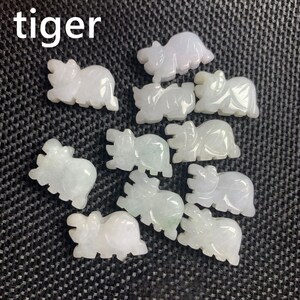 Pode incluir: Uma cole&ccedil;&atilde;o de pequenas figuras de tigre esculpidas em tons de branco e verde p&aacute;lido. A palavra "tiger" est&aacute; impressa em branco no canto superior esquerdo. As figuras est&atilde;o dispostas sobre uma superf&iacute;cie escura e texturizada.