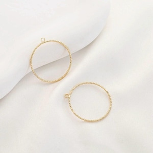 Pode incluir: Dois pingentes circulares de metal dourado texturizado, com pequenas argolas no topo para fazer joias. Os pingentes são redondos com um padrão pontilhado nas bordas. Eles estão em um fundo branco.