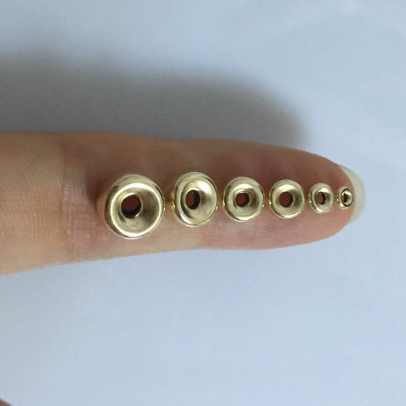 May include: A set of seven gold-colored metal beads with a hole in the center. The beads are arranged in order of size, with the largest bead on the left and the smallest bead on the right.