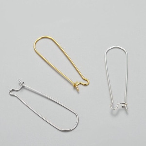 Könnte beinhalten: Zwei Paar Ohrringhaken, einer in Gold und einer in Silber. Die Haken sind oval geformt und haben eine kleine Schlaufe oben.