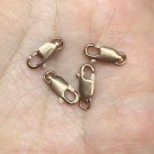 Puede incluir: Cuatro cierres de langosta dorados, un tipo de cierre de joyería utilizado para sujetar cadenas o cordones.