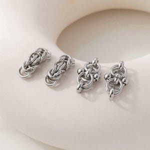 Puede incluir: Cuatro conectores de joyería de metal plateado con un complejo tejido estilo cota de malla. Dos conectores tienen un diseño de eslabones cilíndricos, mientras que los otros dos presentan una estructura similar acentuada con pequeñas cuentas esféricas lisas.