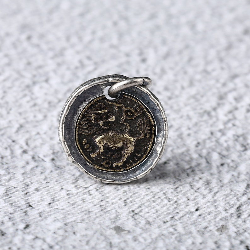 May include: Silver pendant with a round, antique-style design. The pendant features a detailed image of a mythical creature with wings and a tail, set against a textured background.