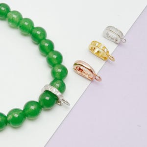 May include: A bracelet made of round green beads with a silver-toned metal bail featuring small clear stones. Three additional metal bails in silver, gold, and rose gold tones are displayed separately, each stamped with the text S925.