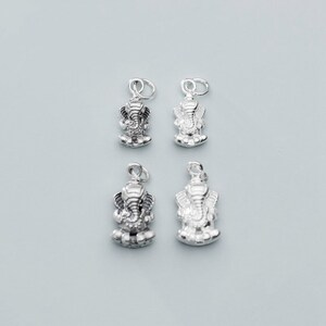 May include: Four silver charms featuring a detailed depiction of the Hindu deity Ganesha, the elephant-headed god of wisdom and good fortune.
