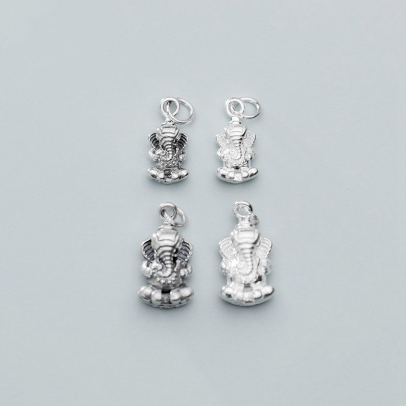 May include: Four silver charms featuring a detailed depiction of the Hindu deity Ganesha, the elephant-headed god of wisdom and good fortune.