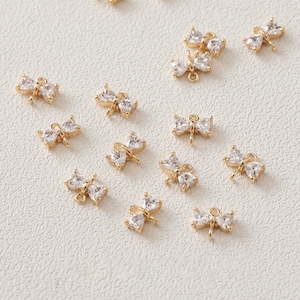 May include: A collection of gold-toned butterfly charms with clear crystal accents. The charms have a loop at the top for attaching to jewelry or other crafts.