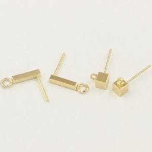 May include: Four gold-toned earring posts, including two rectangular bar designs and two cube designs, each featuring a small circular loop at the top for attaching charms or dangles, presented as individual jewelry components.