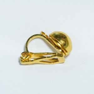 May include: A single gold-colored clip-on earring. The earring features a rounded, domed design and a hinged clip mechanism. The metal has a shiny, reflective surface.