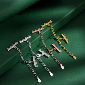 May include: Three multi-strand necklace connectors in silver, rose gold, and gold tones. Each connector features a rectangular bar encrusted with small clear stones, three loops for attaching chains, and an adjustable chain with a lobster clasp.