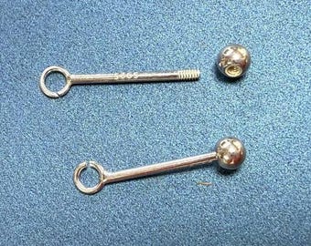 May include: Two silver-colored body jewelry pieces on a blue surface. One piece is a straight barbell with a ball end and a ring end. The other piece is a barbell with a ball end and a threaded post.