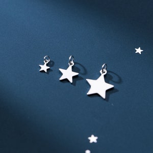 Puede incluir: Tres abalorios de estrella plateados de diferentes tama&ntilde;os. Los abalorios est&aacute;n sobre un fondo azul.