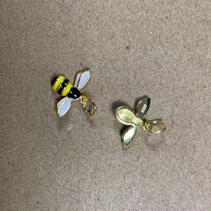 May include: Two gold charms, one shaped like a bee with black and yellow stripes and white wings, the other shaped like a flower with a gold 925 stamp.