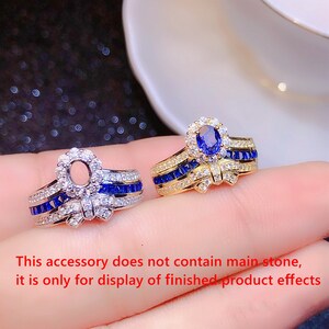 Op de afbeelding: Twee gouden ringen met een strikdesign en blauwe en witte stenen. De ring aan de linkerkant heeft een lege zetting voor een hoofdsteen. De ring aan de rechterkant heeft een blauwe ovale steen in de zetting. Deze accessoire bevat geen hoofdsteen, het is alleen voor de weergave van de effecten van het afgewerkte product.