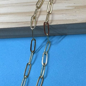 Op de afbeelding: Een gouden ketting met ovale schakels. De ketting ligt plat op een blauw oppervlak.
