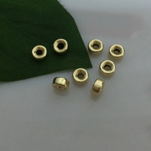 May include: Eight gold-colored metal beads with a hole in the center. The beads are round and have a slightly raised edge.