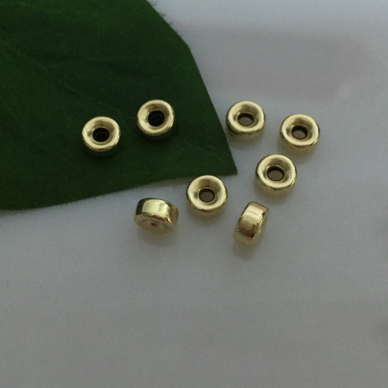 May include: Eight gold-colored metal beads with a hole in the center. The beads are round and have a slightly raised edge.