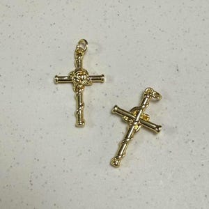 May include: Two gold-tone cross charms with a rose design in the center. The crosses are detailed with a twisted rope design.