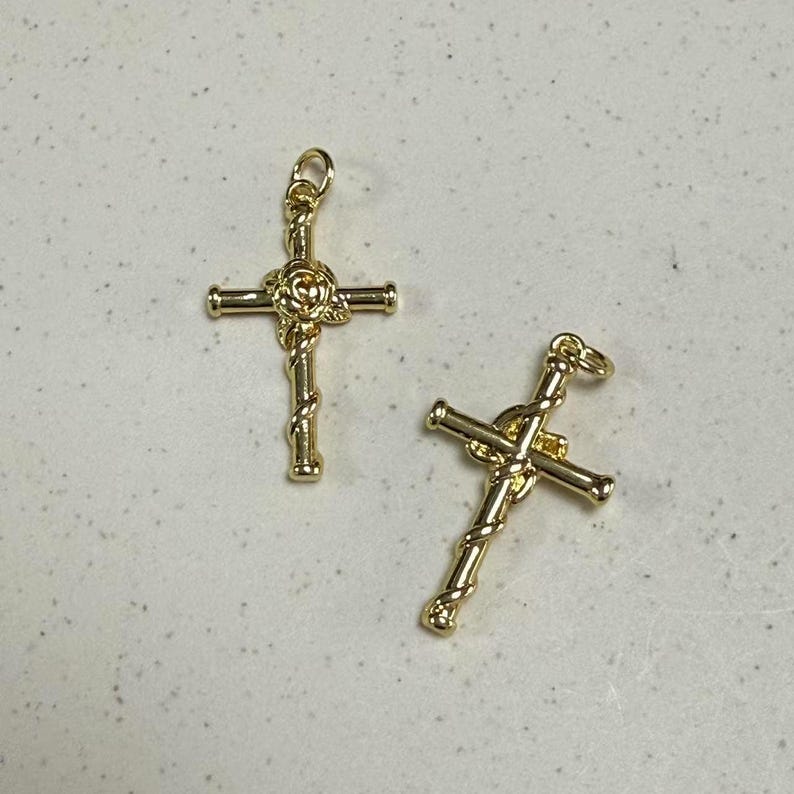 May include: Two gold-tone cross charms with a rose design in the center. The crosses are detailed with a twisted rope design.