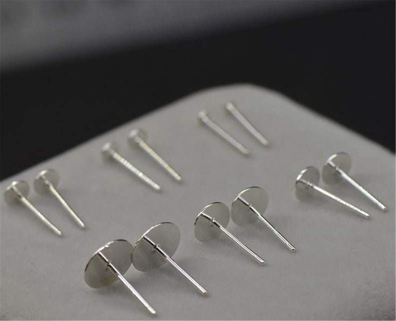 Peut inclure: Un ensemble de tiges d'oreille en argent avec des sommets ronds. Les tiges sont dispos&eacute;es en rang&eacute;e sur une surface blanche.