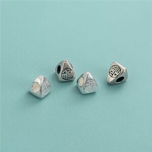 May include: Four silver triangular beads with a Chinese character on each side. The beads have a hole in the center for stringing.