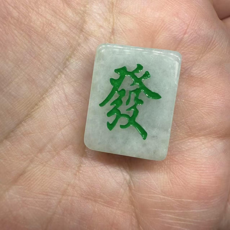 May include: A white mahjong tile with green Chinese characters. The tile is made of a smooth, opaque material.