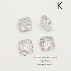 May include: Four silver square beads. Two have a lattice design, and two are covered in small, clear stones. The text indicates the outside diameter is 1.2cm, the hole is 2mm, and the thickness is 6mm. The letter "K" is in the upper right corner.