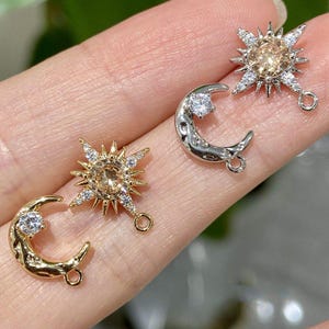 Puede incluir: Dos dijes de estrella de metal con piedras centrales color champán y cristales transparentes, junto a dos dijes de media luna con una piedra transparente. El conjunto incluye acabados en metal de tono dorado y plateado.